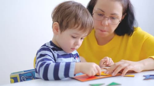 Little Asian Boy Collects Puzzles with Mom Sitting at the Desk A Cute Child Collects a Picture From