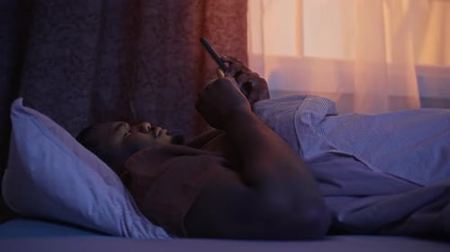 Black Man Lying in Bed Scrolling on Smartphone Late at Night