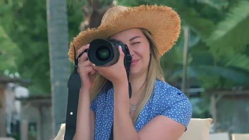 Photographie et voyages Une jeune femme coiffée d'un chapeau tient un appareil photo et prend des photos sur la plage