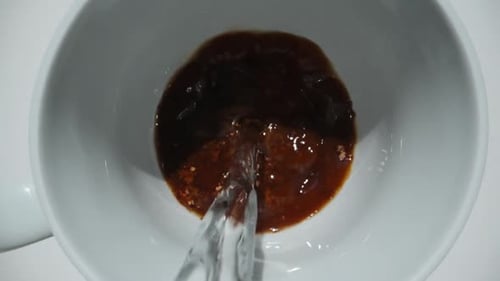 I pour hot water into a mug with instant coffee, slow motion. Dolly slider extreme close-up.