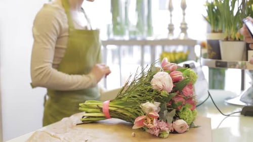 Cheerful florist woman counts bunch cost as man pays with credit card in flower shop