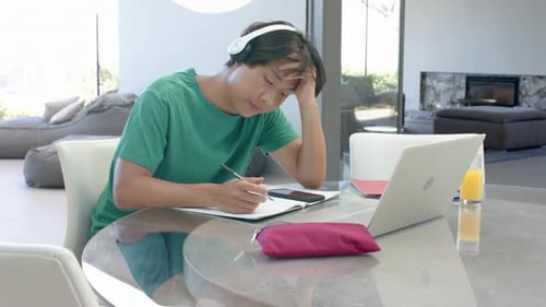 Teenage Asian boy studying on laptop at a modern home setting