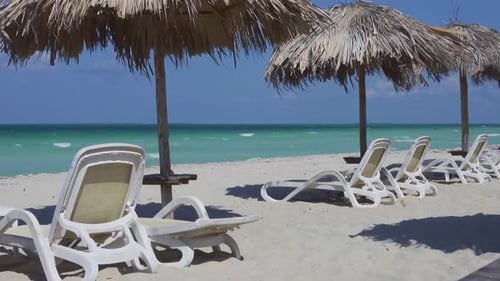 Sand empty beach and straw umbrellas in Varadero, Cuba with white sunbeds and blue ocean, wind and w