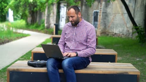Young man works on laptop in city park garden on sunny day