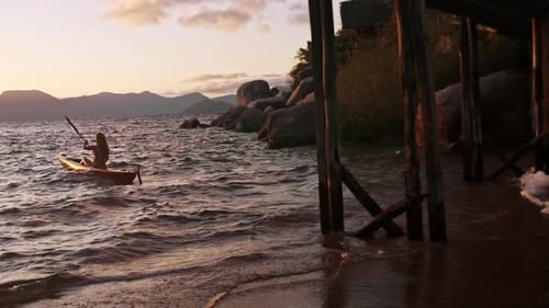 Woman paddling kayak at sunrise on holiday resort lake with sun flare