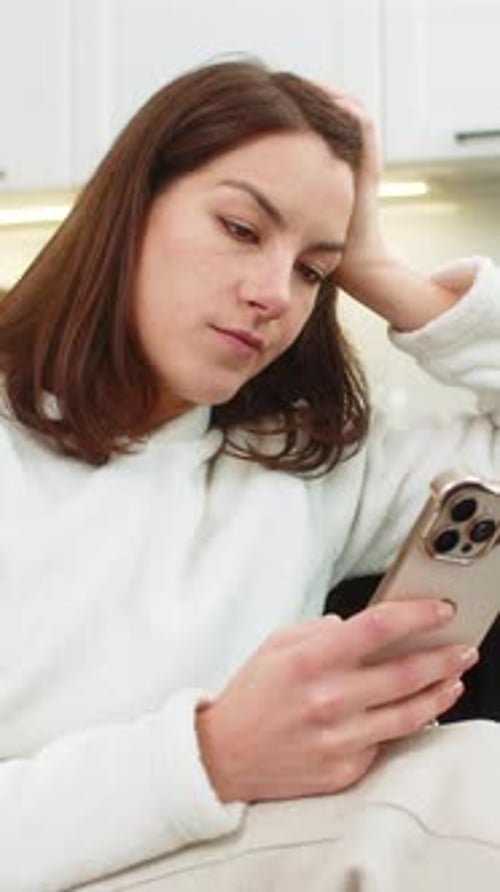 Woman Looks at Phone with Disappointed Expression Indoors