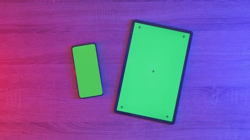 Top down view of mock up green screen smartphone and tablet on an neon desk
