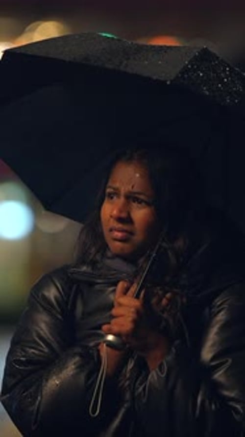 A Woman Dressed in a Raincoat is Holding a Sturdy Umbrella During a Rainy Dark Night