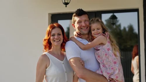 Smiling Family Posing Outside Their Home on Sunny Day