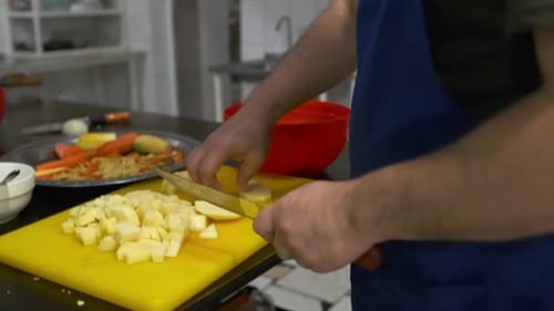 Close-up of a male chef's hands diced peeled potatoes with knife on a yellow cutting board