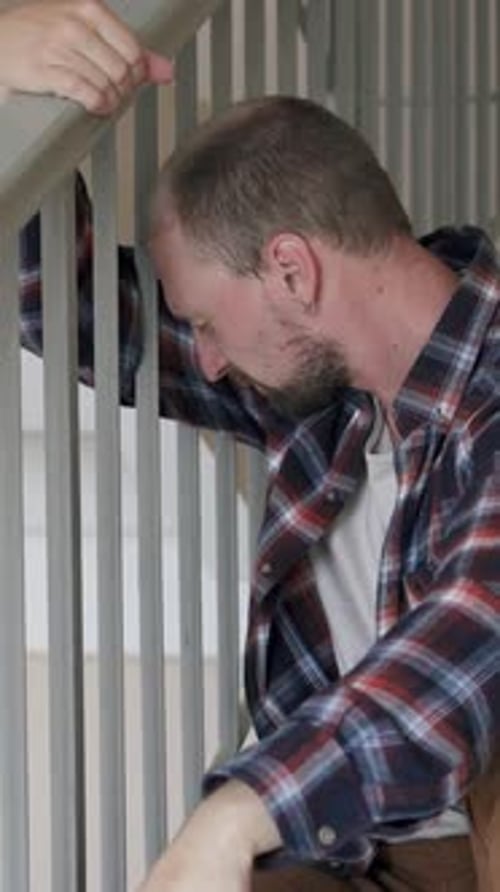 Man Holding Stair Railing Looking Downward in Home
