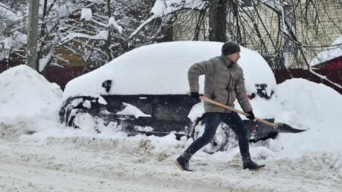 Man Shovels Snow Around Car in Winter