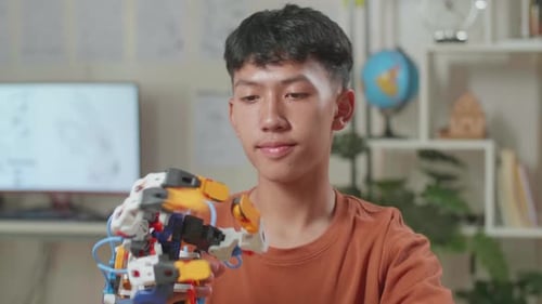 Close Up Of Satisfied Asian Boy Looking And Checking A Cyborg Hand While Working On A Laptop