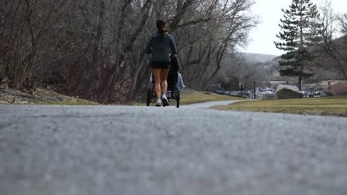 Female Runner Pushing Jogging Stroller on Outdoor Path - Ground-Level View