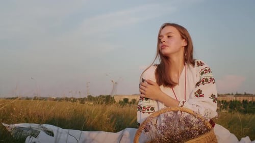Young Woman in Embroidered Blouse Sits in Field
