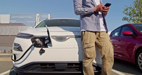 Man Charging Electric Car and Using Smartphone