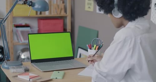 African American Teenage Kid Studying Online Looking at Chroma Key Green Screen Laptop Listening in