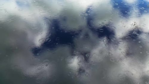 Raindrops on Water Reflecting Cloudy Sky