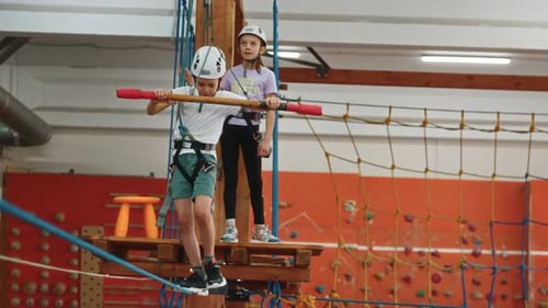 A Little Boy Balances with a Stick and Walks on a Thin Rope in a Rope Park