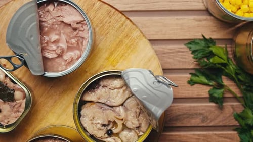 Opening Metal Cans with Canned Fish and Pate on Table Rotating on Wooden Desk Top View Canned Salmon