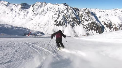 Professional skier racing down a steep ski slope in rythmic short turns. Great mountain view with a