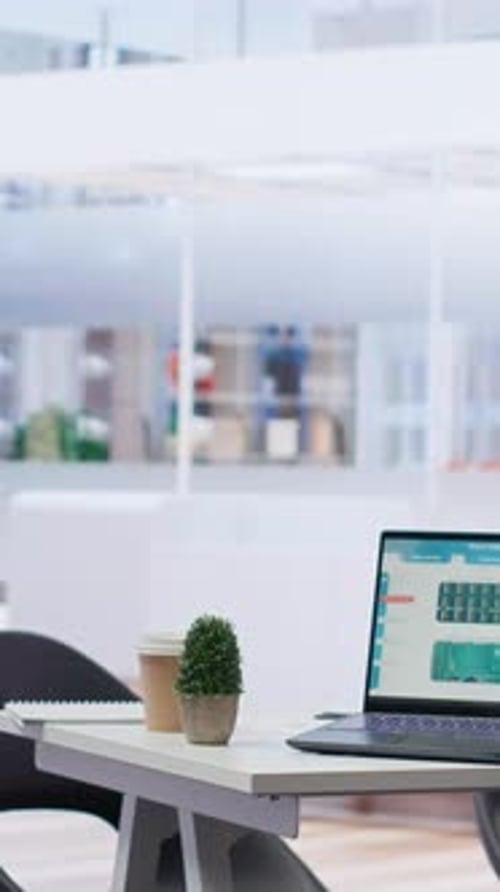 Vertical Video Laptop on Desk Next to Files with Forex Trading Analytics Cityscape Backdrop