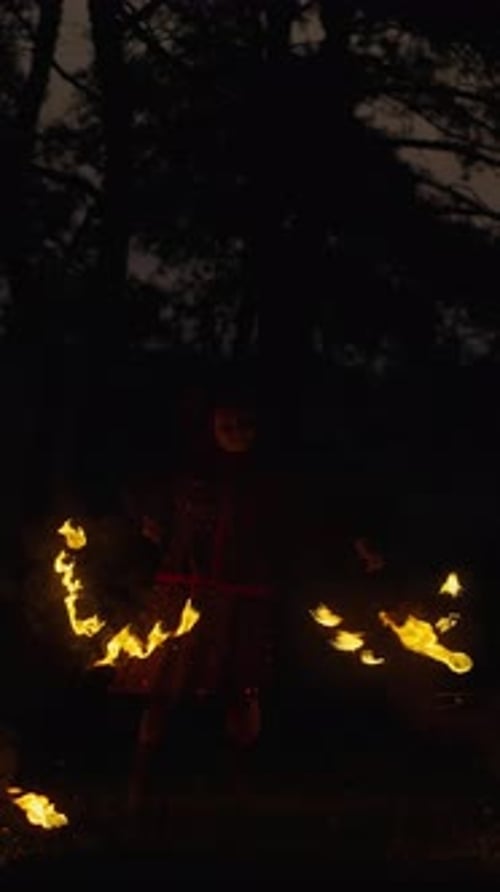 Un mystérieux artiste de feu fait tourner des torches enflammées dans la nuit sombre de la forêt, créant des sentiers tourbillonnants