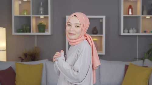 Young woman in headscarf waving and smiling at camera.