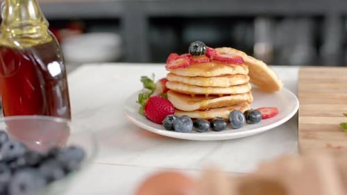 Close up of pancakes with fruits and honey in kitchen, slow motion