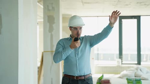 Ingenieur, der ein Walkietalkie benutzt und Arbeitern auf einer Baustelle Anweisungen gibt