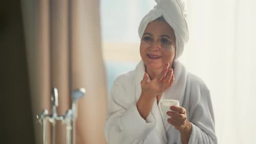 Senior Woman Applying Antiaging Facial Cream on Face Skin in Bathroom Skin Care Selfcare Spa Beauty