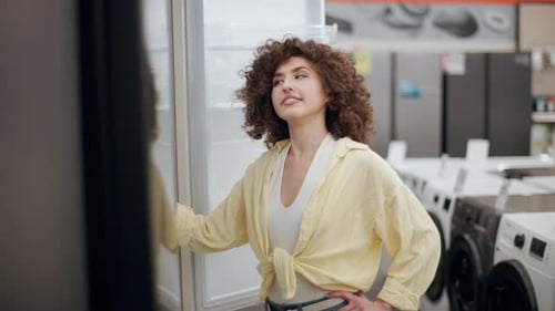 Woman choosing refrigerator in electronics store, slow motion