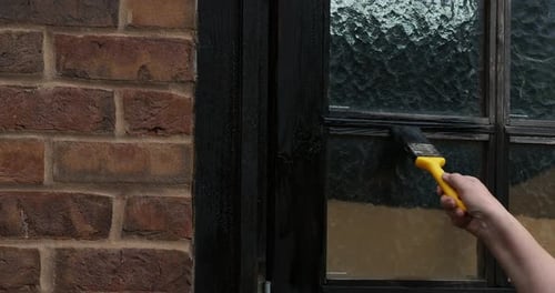 Woman’s hand painting a garage door with wood preservative.
