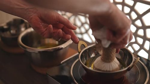 Cropped Shot of Ayurvedic Massage Practitioner Dipping Cottonwrapped Herbal Bundle Into Aromatic Oil