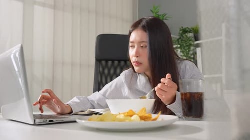 Asian young businesswoman eating noodles while working in the office.