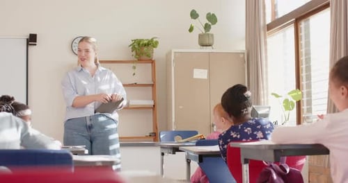 In school, female teacher holding tablet and talking to students in classroom