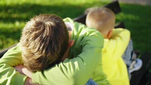 Verärgerte Brüder sitzen nach einem Streit Rücken an Rücken auf der Parkbank
