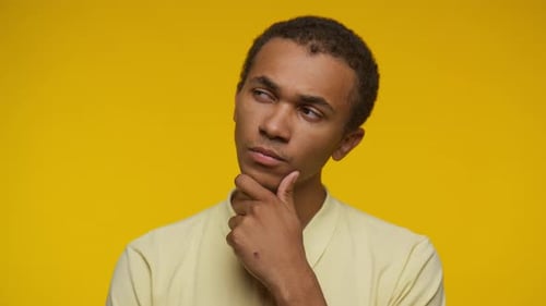Pensive Young Adult Contemplating on Yellow Background