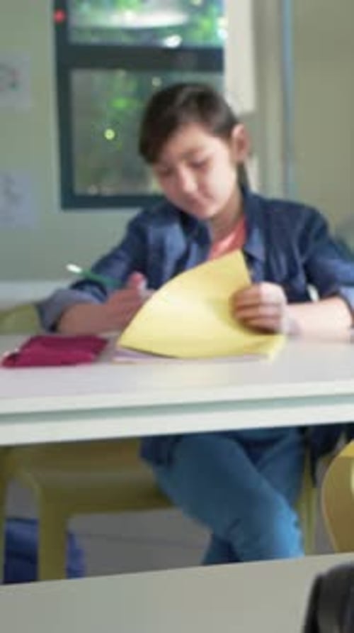 Vertical video: Writing pupil in denim jacket at desk pausing as teacher guiding pencil on notebook