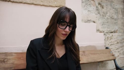 Girl With Glasses Sitting On The Bench In The Village Carefully Reads A Book