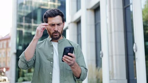 Man Looks Worried at Phone in Urban Setting