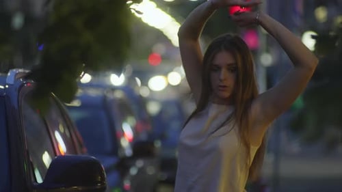 Woman Dancing next to Car on City Street at Night
