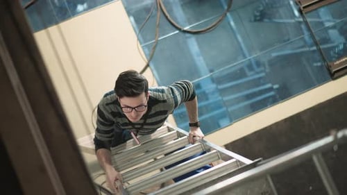 Young Adult Climbing Aluminum Ladder Inside Industrial Building