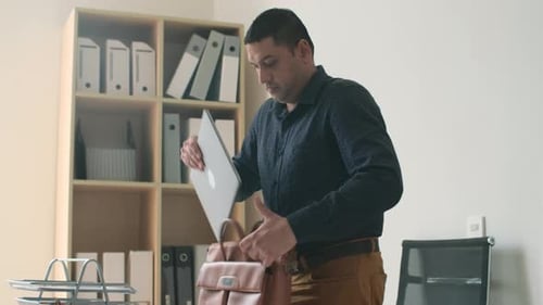 Man Places Laptop on Desk in Office