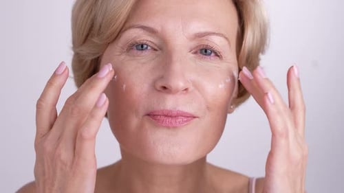 Mature Woman Applies Cream to Face in Close Up