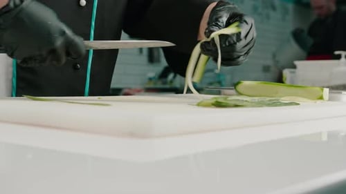 Close-up of a sushi maker in gloves cutting a cucumber with a professional kitchen knife