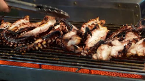 Grilling pieces of squid in a market. Slow motion close up.