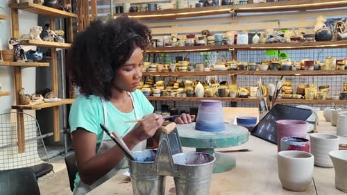 Females potter owners wearing apron sitting and painting a cup ceramics in pottery studio.
