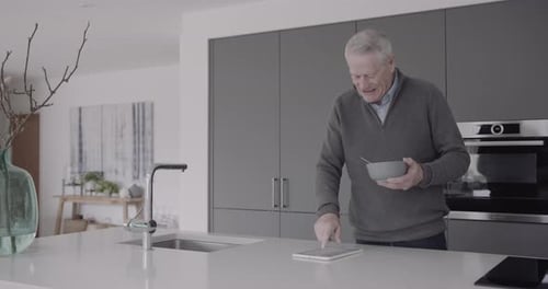 Man Eating Cereal while Using Tablet in Kitchen