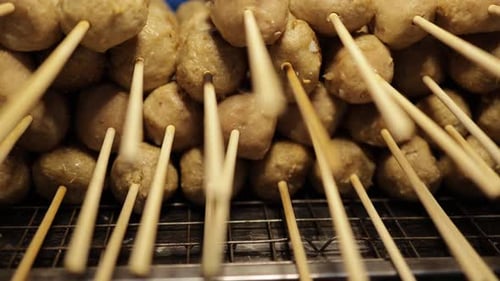 Close-up, panning shot of grilled meatball on skewers stacked on hot charcoal grill at street food s